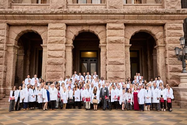 Group of doctors in white lab coats standing on steps in front of Texas Capitol building.